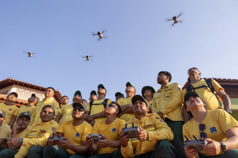 Indigenous fire brigades flying drones donated by EJF, with their bright yellow uniforms contrasting against a clear blue sky.