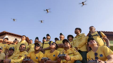 Indigenous fire brigades flying drones donated by EJF, with their bright yellow uniforms contrasting against a clear blue sky.